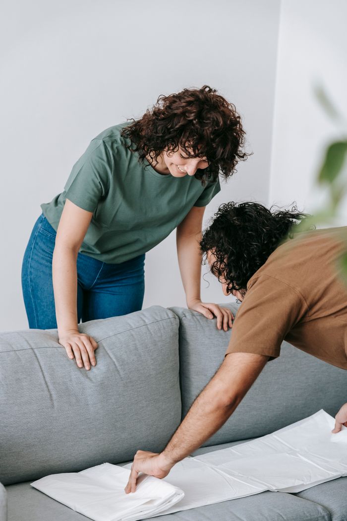Couple getting the living room ready by draping the sofa with a white protective sheet.